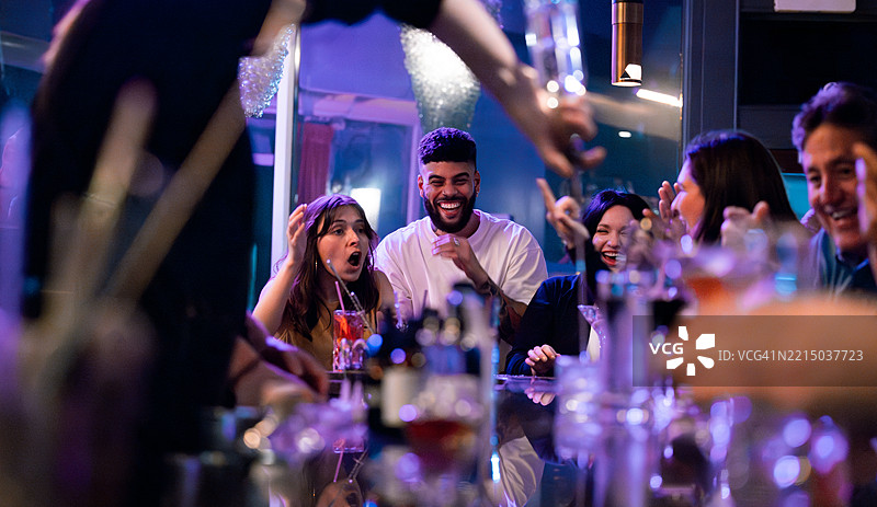 一群人在现代高档酒吧里兴奋地欢笑和交谈。图片素材