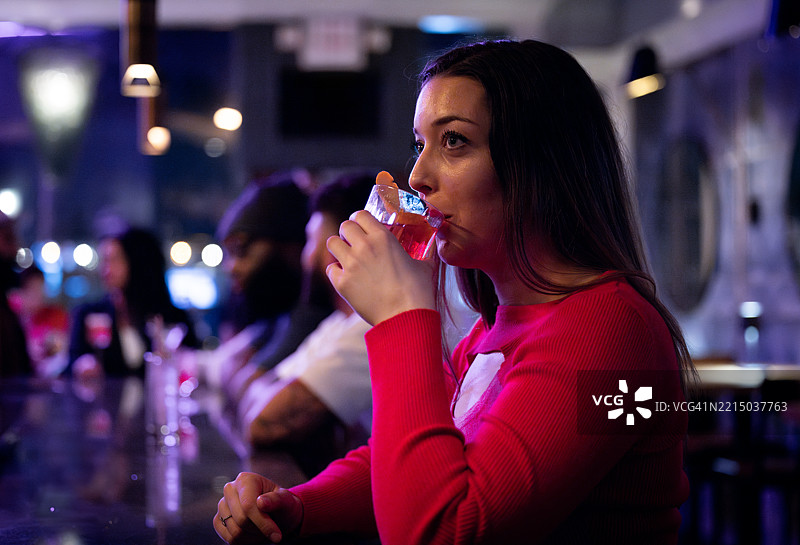 一位女性坐在时尚昏暗的酒吧里，品尝着色彩鲜艳的鸡尾酒。图片素材