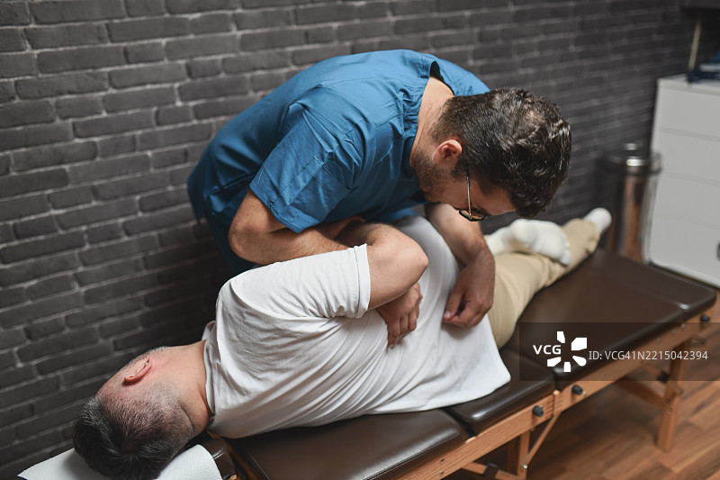 男性患者侧卧，脊医正在进行脊柱调整。图片素材
