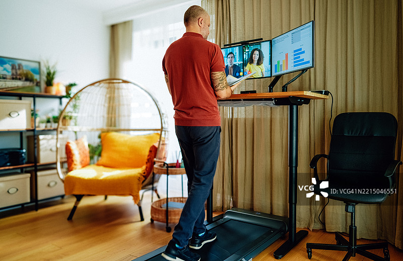 商人在跑步机上走路，同时与同事进行视频通话。图片素材