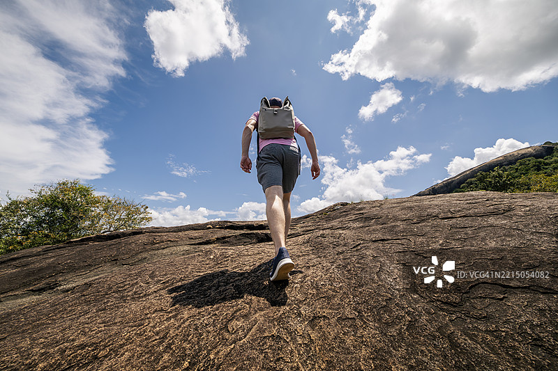 男子背着背包攀登岩石顶部图片素材