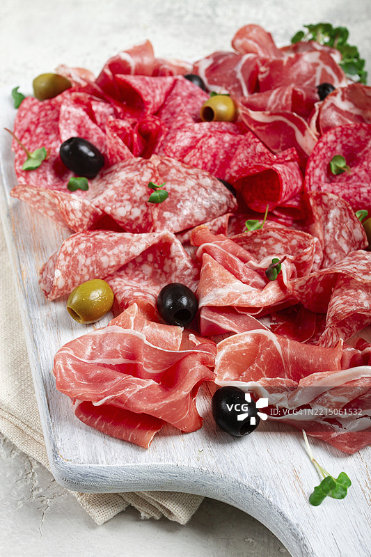 各种肉类开胃菜，包括火腿、萨拉米香肠和火腿，搭配橄榄，放在白色木板上，背景明亮，早餐，俯视图，特写，无人。图片素材