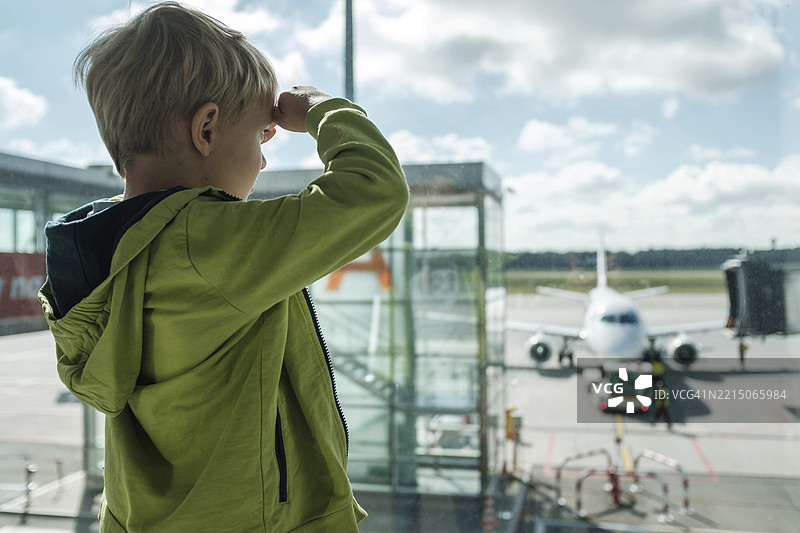 小男孩在机场透过窗户向外看图片素材