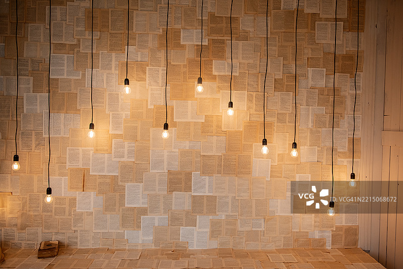 墙壁和台阶上铺满了打开的书籍，悬挂的灯泡照亮了它们。图片素材