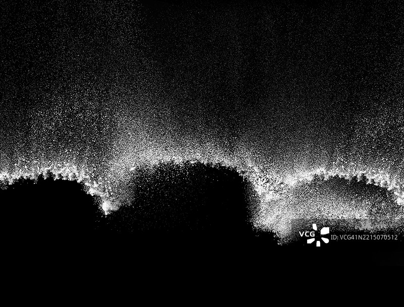 波浪形的白色尘埃颗粒在黑色背景下飘落。图片素材