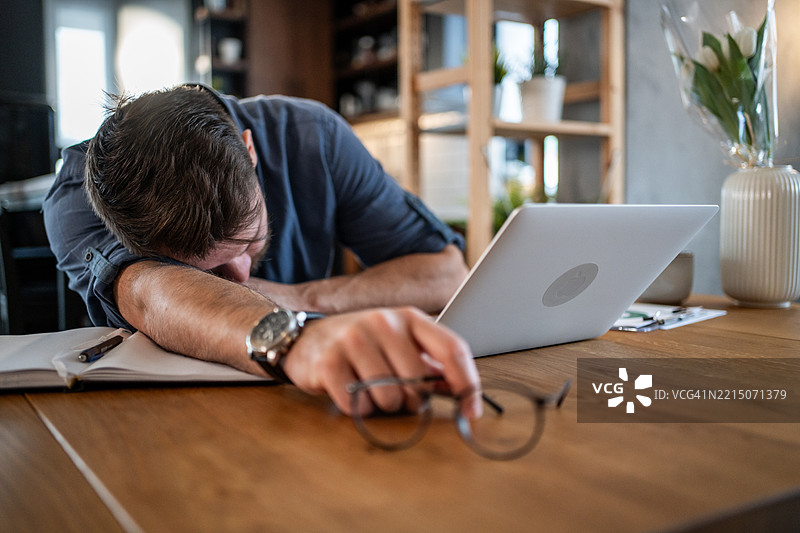疲惫的商人在家中桌子上睡觉，因在笔记本电脑上工作而感到疲惫图片素材