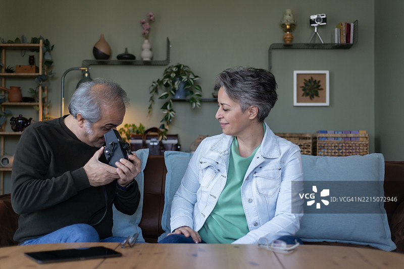 两位退休老人坐在沙发上研究一台复古相机。他们准备拍几张照片。图片素材