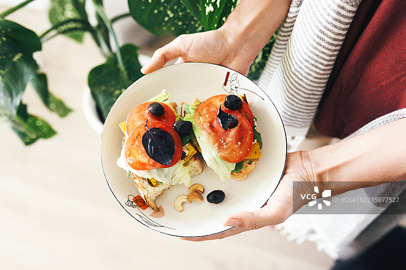 手中拿着装有番茄吐司和叶子装饰的盘子图片素材