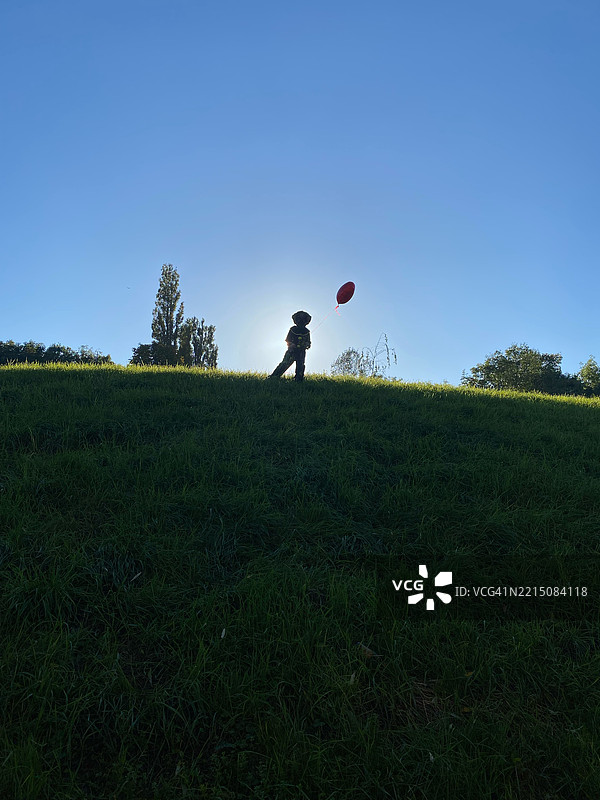 在草坡上，孩子的剪影手持红色气球，伦敦，英国图片素材