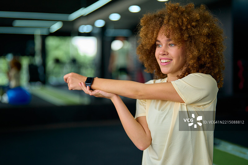 年轻女性在健身房伸展手臂并查看智能手表图片素材