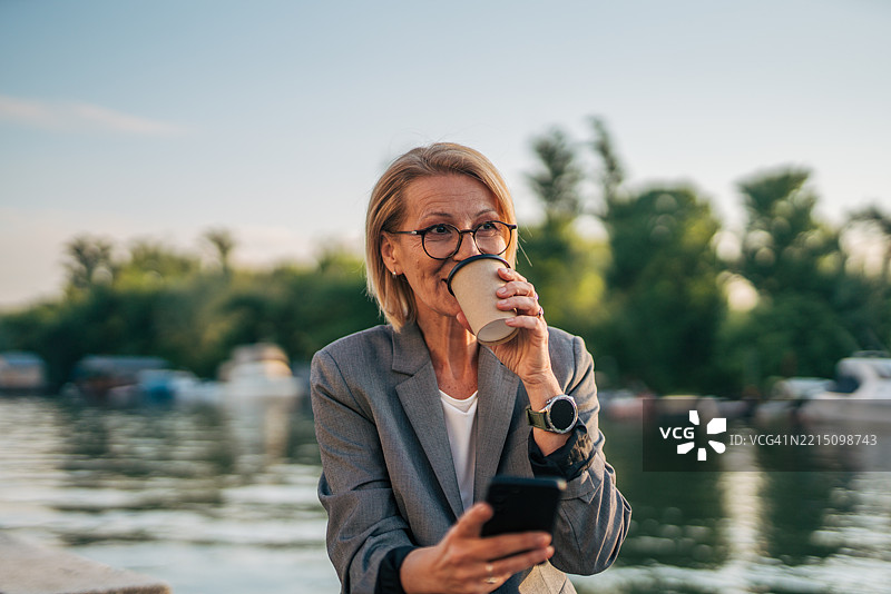 在河边喝咖啡并使用智能手机的女商人图片素材