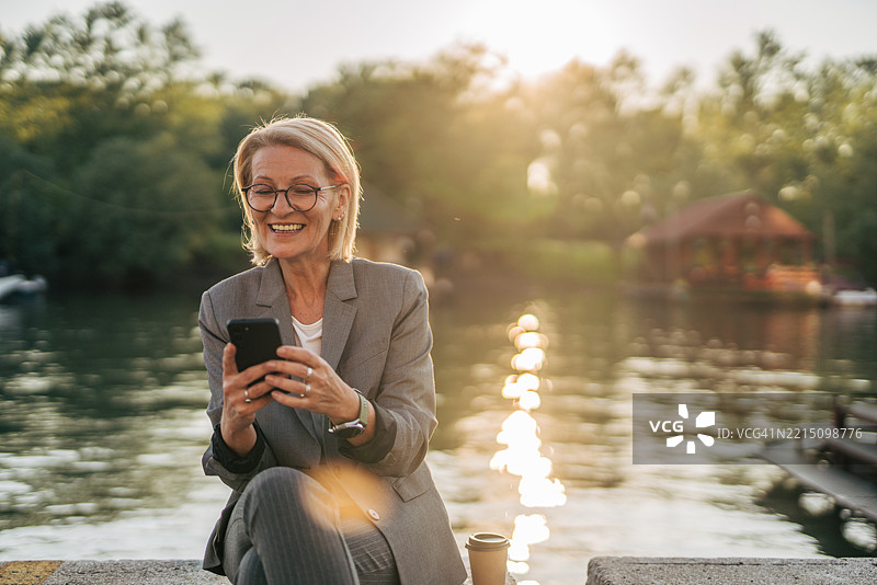 湖边日落时分，一位资深女商人正在使用智能手机图片素材