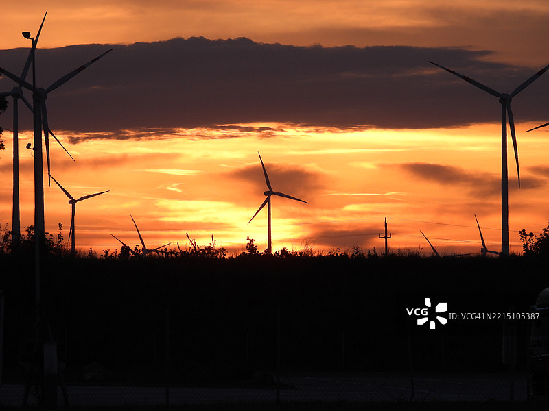 日落时分，天空下田野上的风力涡轮机剪影图片素材