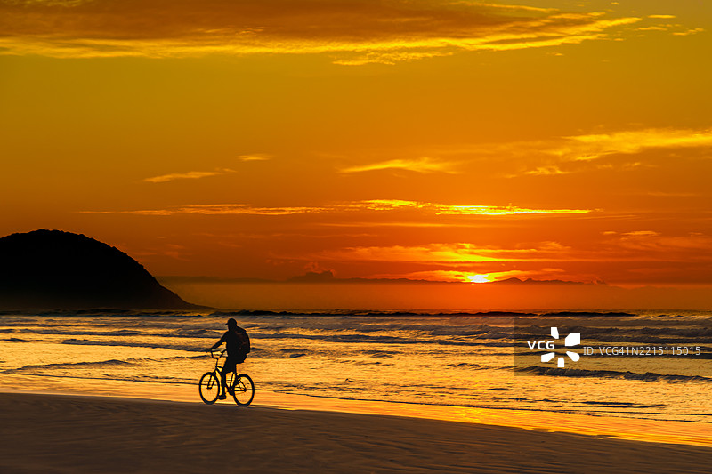 日落时分，巴西贝尔季奥加海滩上骑自行车的男子剪影图片素材