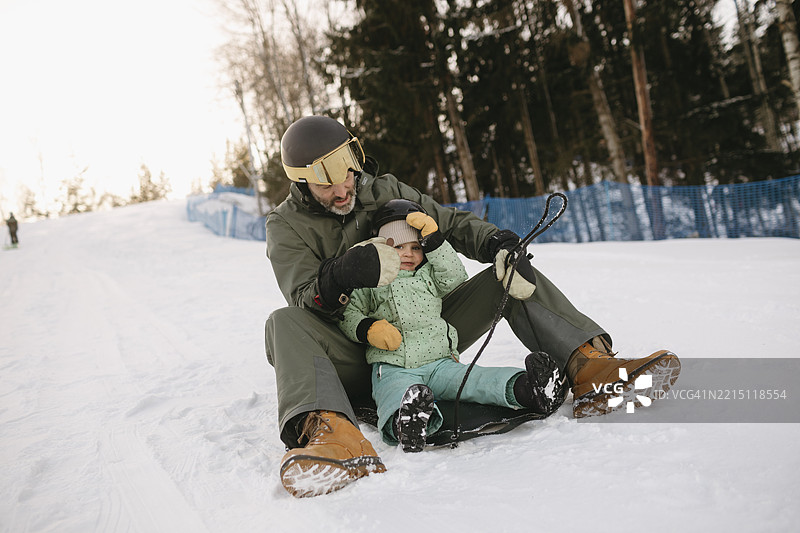 父亲和女儿在滑雪度假村的雪地上悠闲地坐着。图片素材
