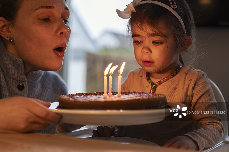 母女俩在家中一起吹生日蛋糕上的蜡烛的特写镜头图片素材