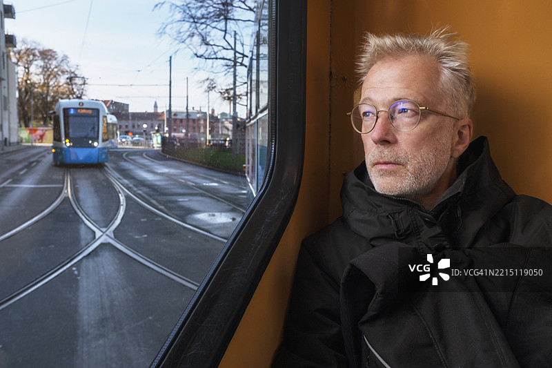 沉思的老年男子坐在缆车里透过窗户望外。图片素材
