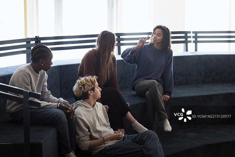 年轻女性在校园的沙发上与朋友讨论时做手势图片素材