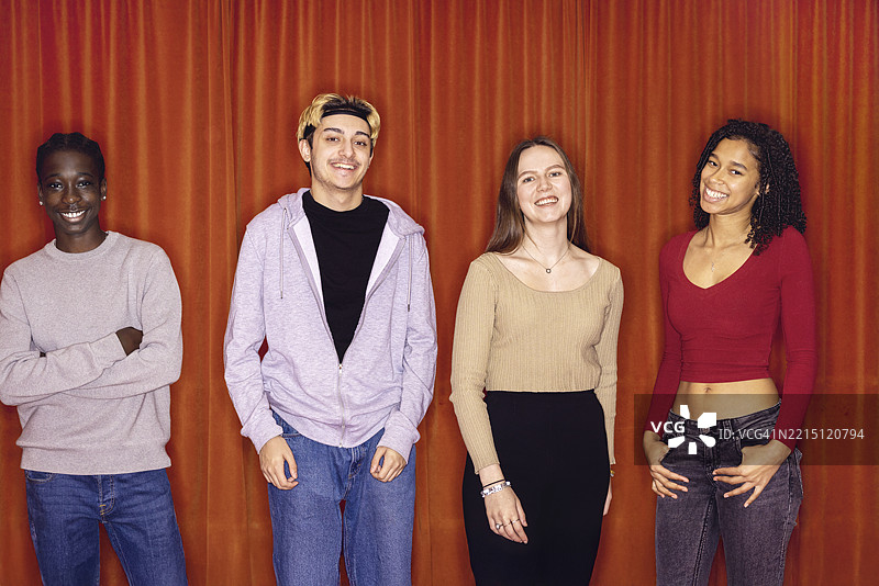 快乐的多种族男女朋友站在红色幕布前的肖像图片素材