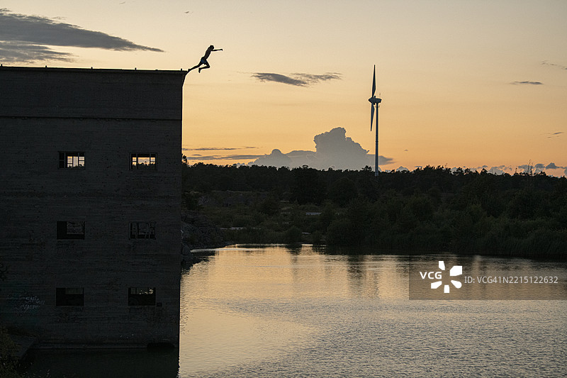 一个无法辨认的人在日落时分从废弃建筑的顶部跳入水中图片素材
