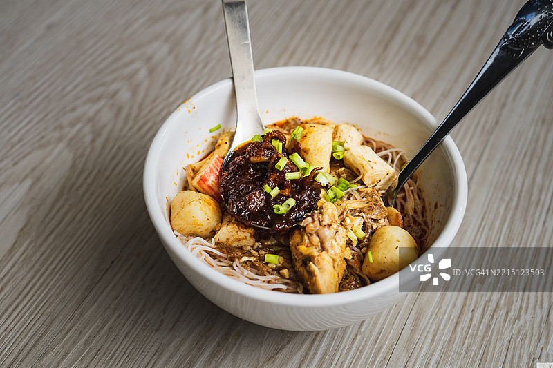 马来西亚椰浆米粉汤，碗中盛有鸡肉、虾和豆腐，背景为木质桌面图片素材