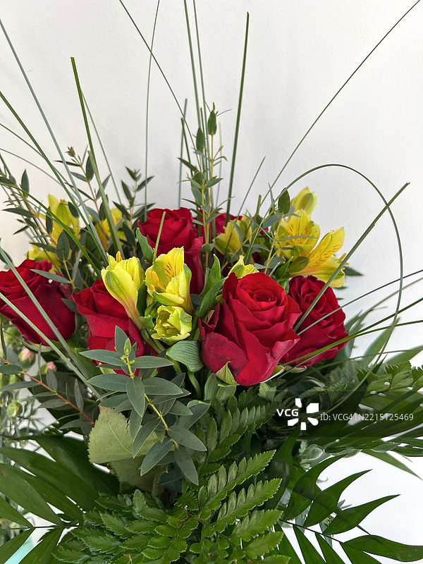 鲜艳的红玫瑰和黄色花朵的花束，配以绿色叶子图片素材