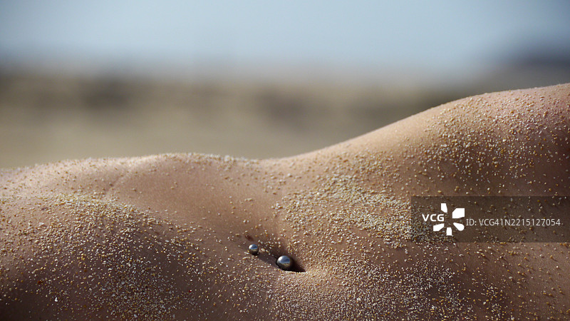 赤裸上身的女性中部，沾满湿沙和穿孔饰品图片素材