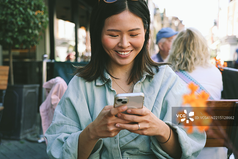 微笑的年轻女性在户外咖啡馆看手机图片素材