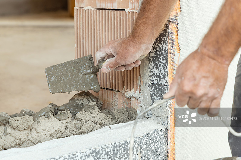肮脏的工匠手用抹子将水泥或石膏涂抹在墙上，特写建筑细节图片素材