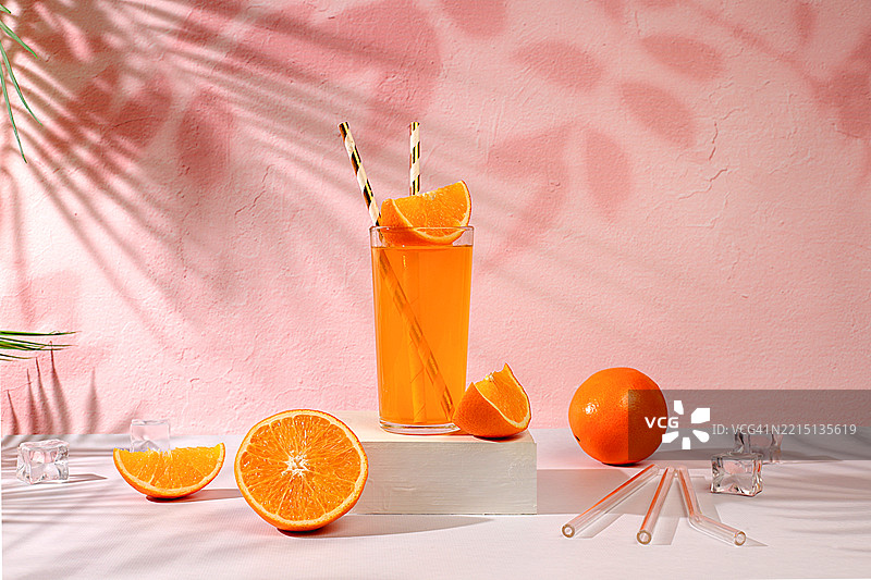 现代静物作品，粉色背景上的柑橘水果、橙汁和橙子，长长的硬影，极简排毒饮食概念，夏季维生素饮品，选择性焦点图片素材