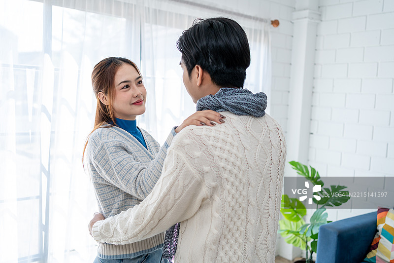 亚洲年轻夫妇在冬季的家中享受温馨时光。迷人的配偶，夫妻俩在音乐中跳舞，感到快乐和放松，舒适地站在家中的客厅里。图片素材