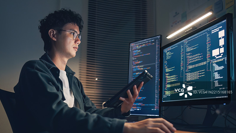 戴眼镜的白人程序员或IT专家软件开发人员在深夜工作，查看移动应用的用户体验和用户界面流程图及设计线框图，在双显示器电脑上整合设计与开发。图片素材