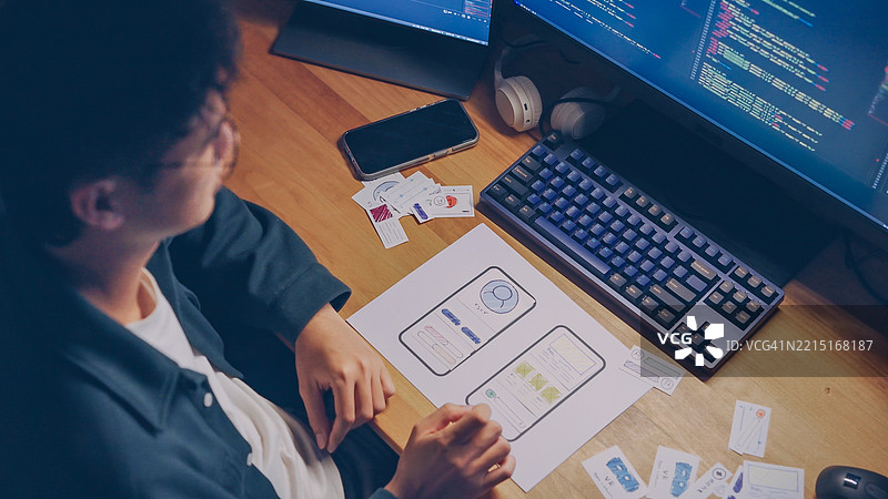 UX开发者在深夜加班时，特写镜头展示其在纸质原型上排列移动应用UI/UX设计元素，正在制作线框图或纸质原型。图片素材