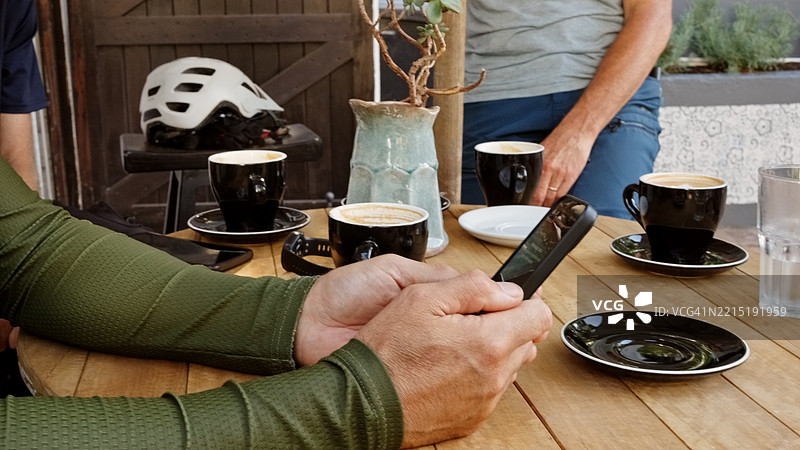 男子在咖啡馆里使用手机，桌上有咖啡和自行车头盔的特写镜头图片素材