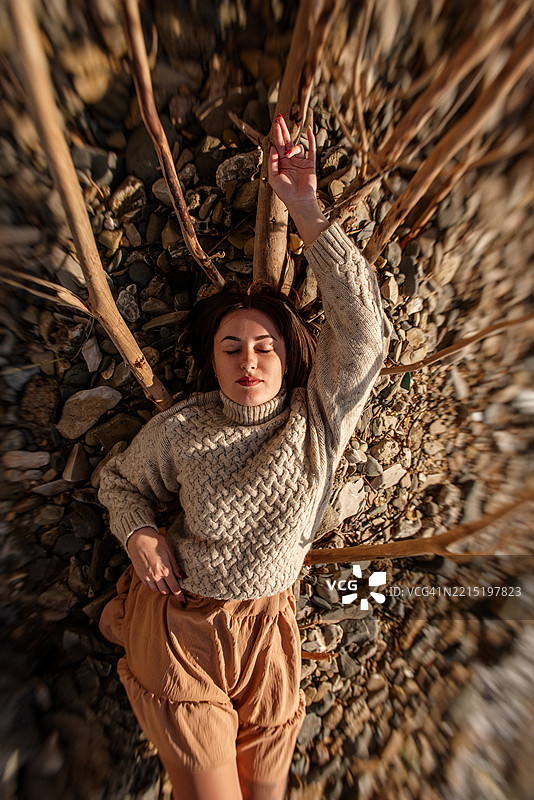 年轻女性躺在有漂流木的岩石海滩上图片素材