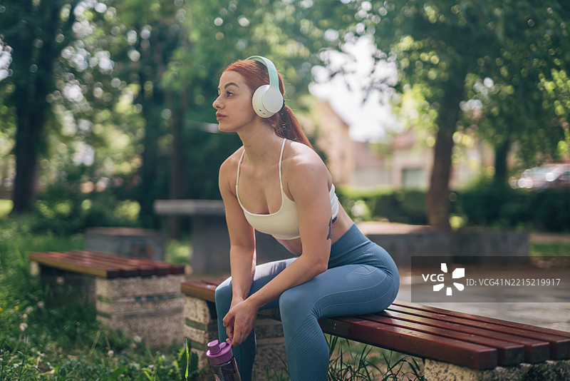 年轻女运动员在训练后放松，坐在长椅上戴着耳机听音乐图片素材
