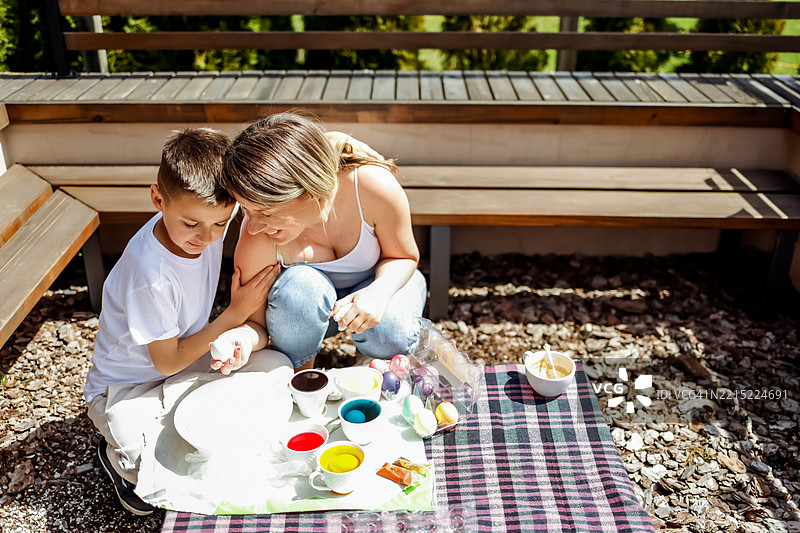 母亲和儿子在阳光明媚的户外桌子上一起涂彩蛋图片素材