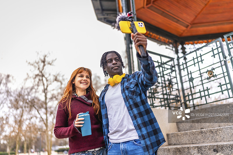 两位内容创作者在城市公园进行视频博客，使用专业设备如智能手机稳定器和麦克风制作高质量视频。图片素材