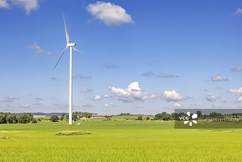在阳光明媚的夏日，瑞典乡村的美丽风景中，一座高大的风力涡轮机矗立在田野上。图片素材