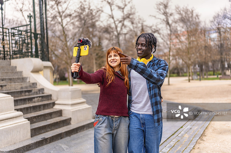 两位年轻的内容创作者在公园里用附有麦克风的智能手机录制他们的 vlog 视频。图片素材