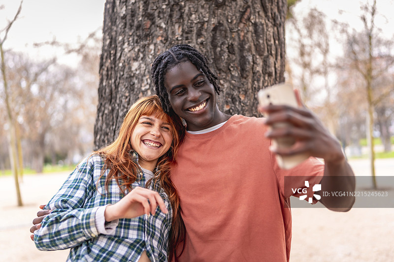 年轻的多种族情侣在公园里用智能手机自拍，面带微笑，享受快乐时光图片素材