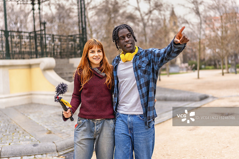 两个微笑的内容创作者在公园里工作，使用吊杆麦克风和耳机录音。图片素材