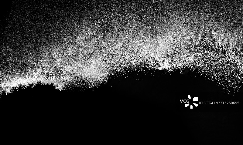 白色尘埃颗粒形成波浪状，向下飘落在黑色背景上。图片素材