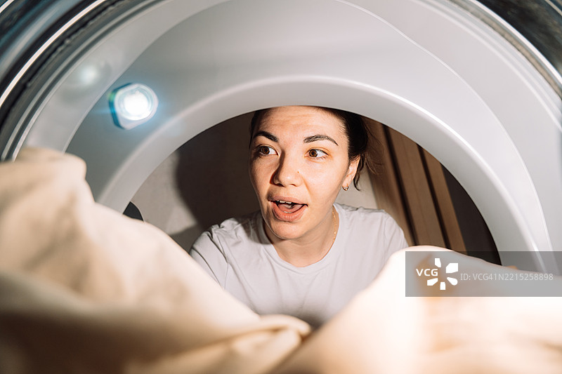 惊讶的女人从洗衣机或烘干机内部看，里面是干净的衣物图片素材