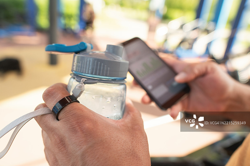 户外健身房中佩戴智能戒指和使用智能手机的男子图片素材