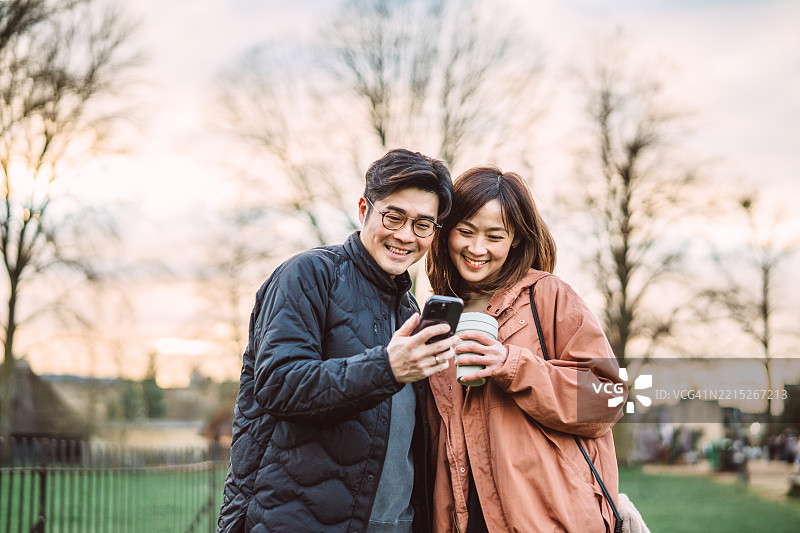 快乐的亚洲情侣在风景如画的公园里一起享受手机内容图片素材