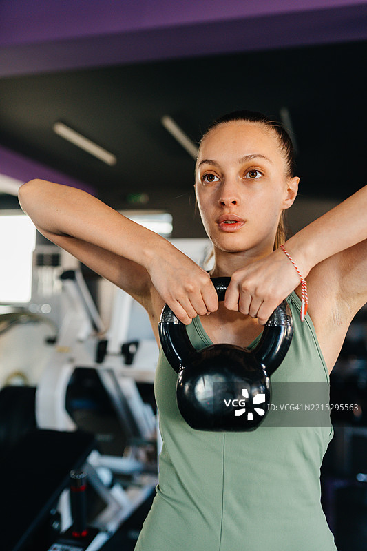 一位年轻女性在健身房用双手举起壶铃图片素材