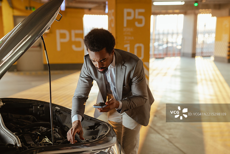 男子在停车场修理汽车发动机，同时使用手机图片素材