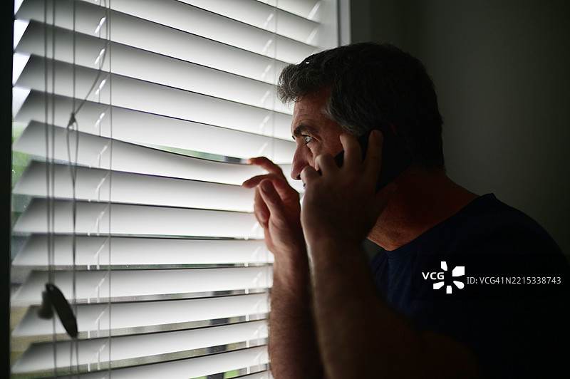 男子透过窗户怀疑邻居，秘密拨打政府热线。图片素材