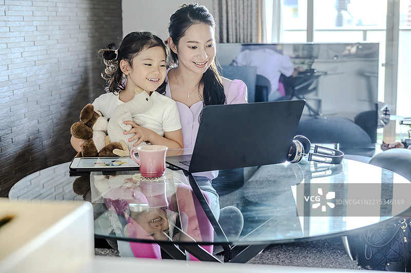 微笑的母女俩一起坐在沙发上看笔记本电脑图片素材